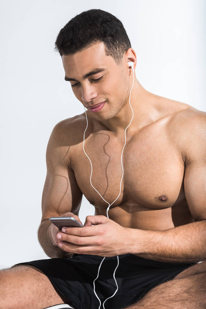 handsome athletic man with smartphone listening music and smiling on white - Foto, immagini