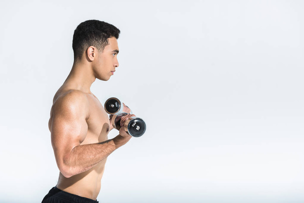 side view of shirtless mixed race man training with dumbbells on white - Foto, Imagem