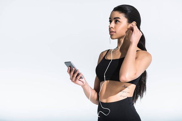 attrayant sportif afro-américain fille tenant smartphone et écouter de la musique dans les écouteurs sur blanc
 - Photo, image