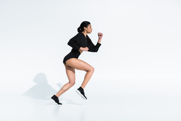 vista lateral de la hermosa chica afroamericana deportiva en ropa deportiva negro corriendo en blanco
 - Foto, imagen