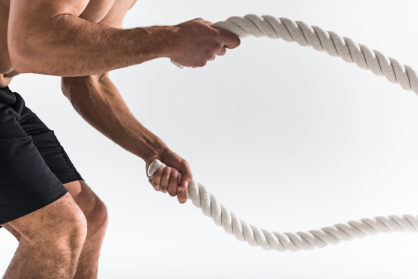 partial view of sportive man doing exercise with ropes on white background  - Photo, Image