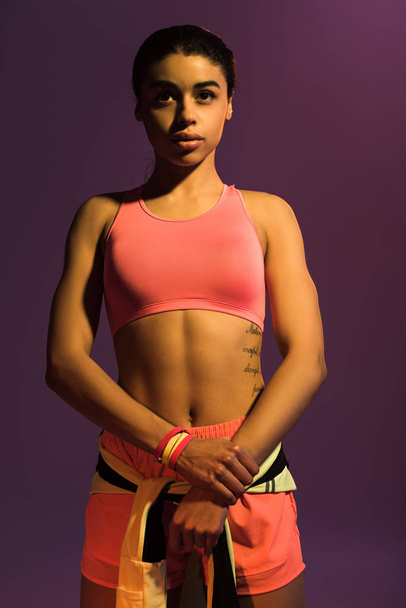 αρκετά αθλητικός Αφρικανός Αμερικανός κορίτσι σε ροζ αθλητικό σουτιέν απομονώνεται σε μωβ - Φωτογραφία, εικόνα