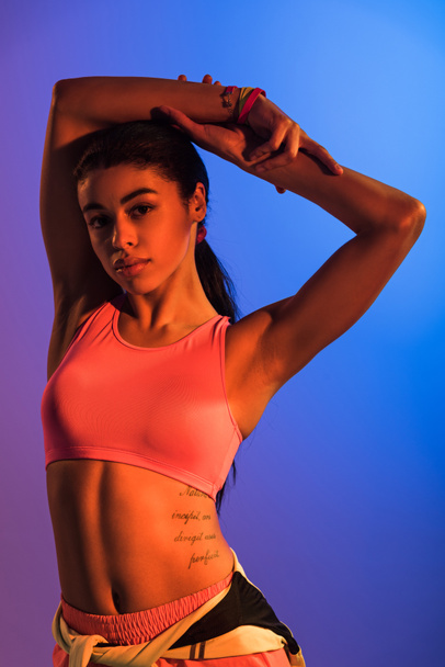 beautiful athletic african american girl in pink sports bra posing at camera on purple and blue gradient background - Фото, зображення