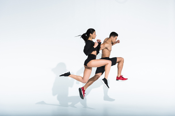 oldalsó kilátás a sportos multikulturális nő és férfi a sportruházat és a cipő futó fehér alapon - Fotó, kép