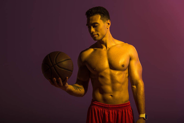 Красивый спортсмен смешанной расы держит коричневый мяч на фиолетовом фоне
 - Фото, изображение