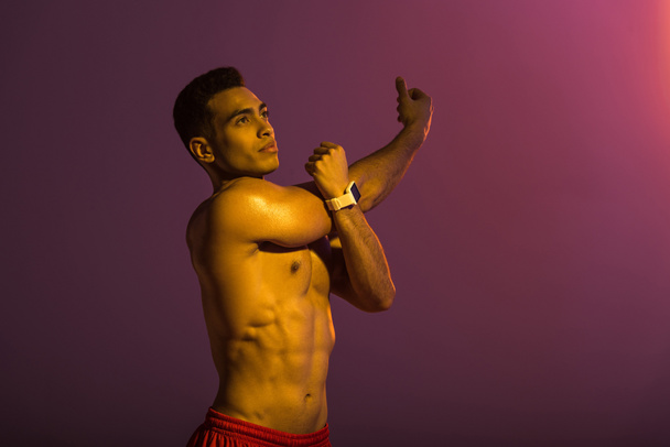 handsome sportive man in smart watch stretching on purple background - Фото, зображення