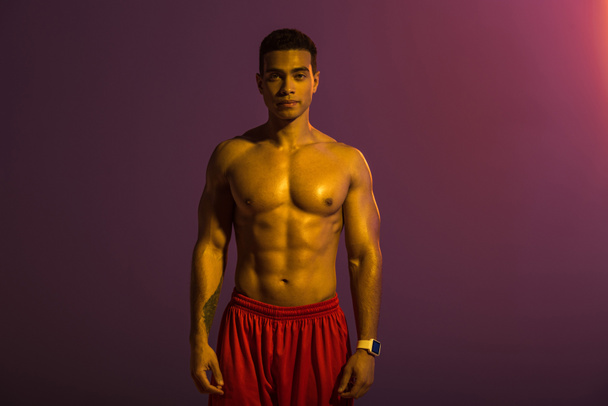 urheilullinen sekarotuinen mies, jolla on lihaksikas vartalo ja joka katsoo kameraa violetilla taustalla
 - Valokuva, kuva