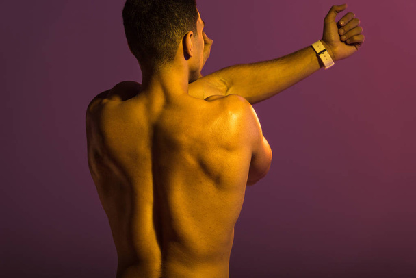 back view of athletic man with muscular torso stretching on purple background - 写真・画像
