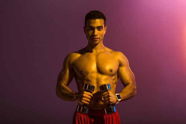 guapo deportivo mestizo hombre de raza sosteniendo mancuernas sobre fondo púrpura
 - Foto, imagen