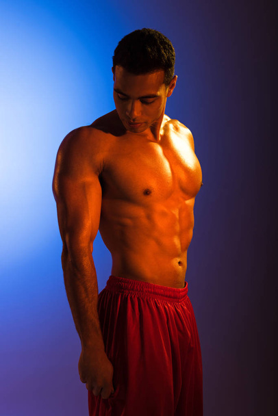 handsome sportive mixed race man with muscular torso posing at camera on blue and dark purple gradient background - Foto, imagen