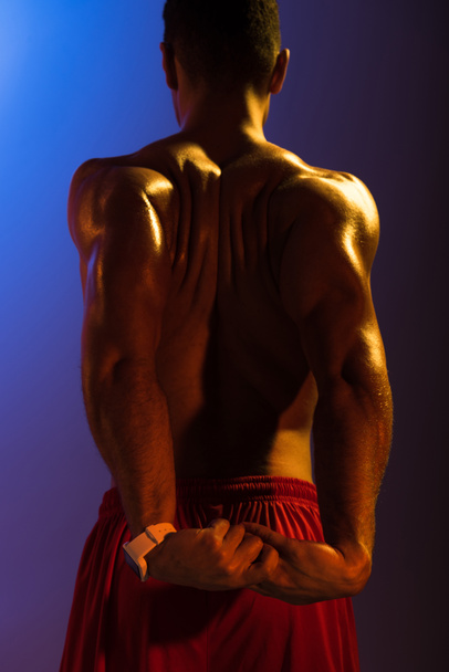 pohled na atletického muže se svalovým trupem natažným na modrém a tmavém purpurovém pozadí - Fotografie, Obrázek