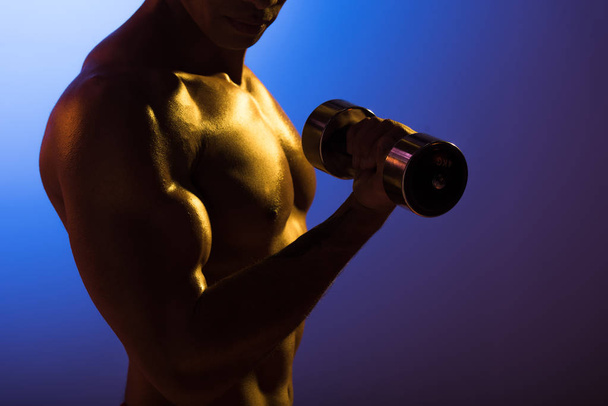 cropped view of athletic man with dumbbell on blue and dark purple gradient background - Фото, изображение