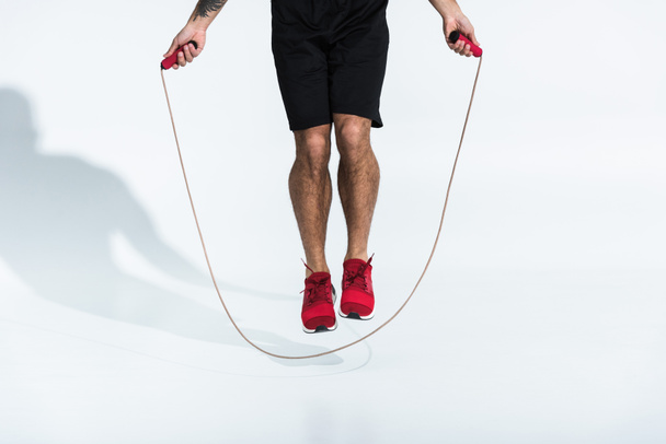vista parziale dell'uomo in pantaloncini neri e scarpe da ginnastica rosse che saltano con corda da salto su bianco
 - Foto, immagini