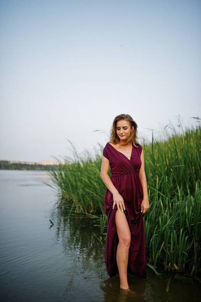 Loira sensual mulher em vermelho marsala vestido de pé na água de l
 - Foto, Imagem