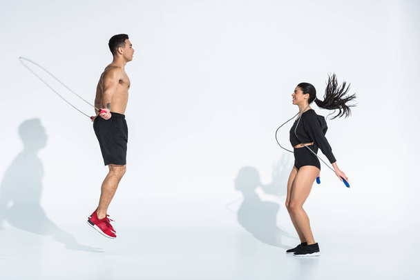smiling african american woman and athletic mixed race man training with jump ropes on white - Photo, Image