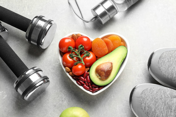 Heart shaped bowl with healthy products and sports equipment on grey background, flat lay - Photo, Image