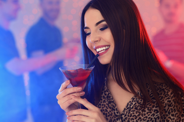 Beautiful young woman with glass of martini cocktail in bar, space for text - Фото, изображение