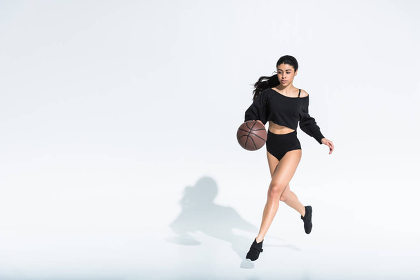 красива афроамериканська дівчина в чорному спортивному одязі і кросівки біжить і грає в м'яч на білому
 - Фото, зображення