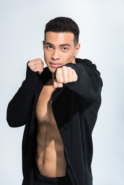 handsome mixed race man in black sports jacket warming up and looking at camera on white - Photo, Image
