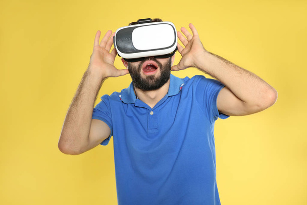 Emotional young man playing video games with virtual reality headset on color background - Foto, Imagem