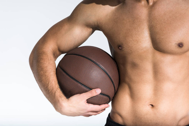 przycięte widok sportowiec z mięśni tułowia trzymając brązowy piłkę na białym - Zdjęcie, obraz