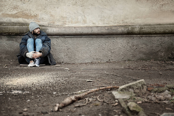 Poor homeless man sitting near wall on street. Space for text - Photo, image