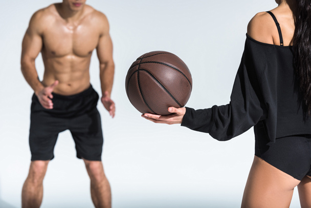 vista ritagliata di uomo senza maglietta con busto muscolare vicino sportivo ragazza africana americana in possesso di palla su bianco
 - Foto, immagini