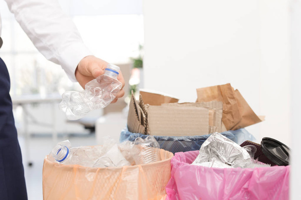 Man putting used plastic bottle into trash bin in office, closeup. Waste recycling - Φωτογραφία, εικόνα