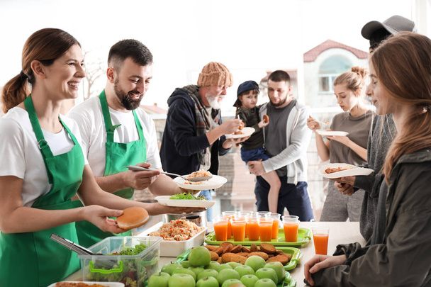 Volunteers giving food to poor people indoors - Fotó, kép