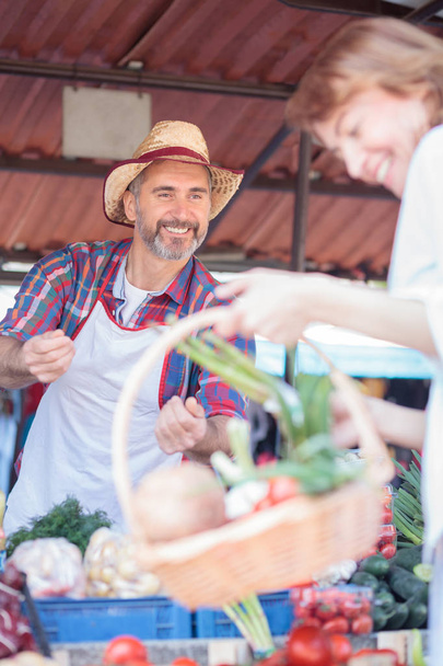 Ευτυχισμένος ώριμος αγρότης πουλώντας φρέσκα βιολογικά λαχανικά σε μια αγορά - Φωτογραφία, εικόνα