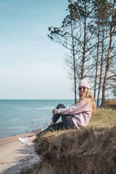 Pembe şapkalı genç bir kadın kayalıklarda tek başına oturuyor, deniz, özgürlük konsepti, huzurlu atmosfer, meditasyon, fotokopi alanı, Letonya, Jurkalne - Fotoğraf, Görsel