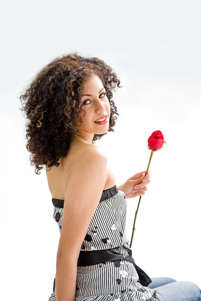 Sincere beautiful young woman with brown curly wild hair and bare shoulders holding red rose, isolated - Foto, Imagem