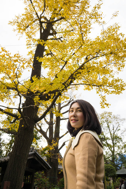 イチョウの木を背景にアイリーンの肖像画撮影、秋は葉が黄色になり、魅惑的な開花草原を体験. - 写真・画像