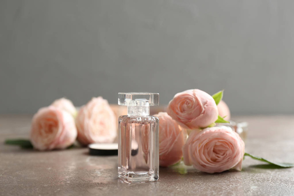 Bottle of perfume and roses on table against grey background - Фото, зображення