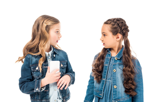 duas crianças surpresas com smartphone olhando um para o outro isolado no branco
 - Foto, Imagem
