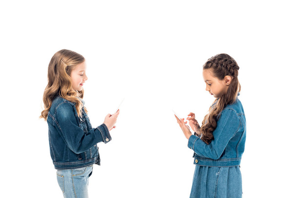 zwei Kinder in Jeanskleidung mit Smartphones isoliert auf weiß - Foto, Bild