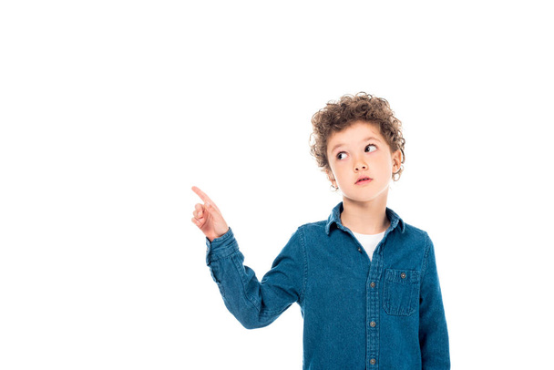 pensive curly kid in denim shirt pointing with finger isolated on white - Photo, Image