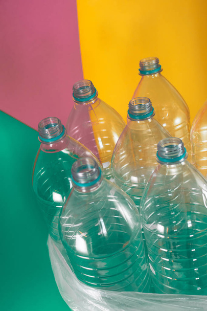 Um pacote de 7 garrafas de água de plástico vazias e recicláveis, sem tampas, selo azul, em um saco de plástico, em tons pastel coloridos de fundo verde marinho, rosa suave e amarelo. Reutilização, Eco-Friendly
 - Foto, Imagem
