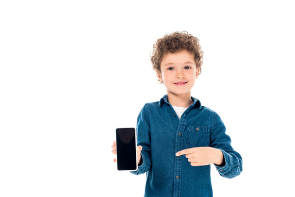 front view of curly child in denim shirt pointing with finger at smartphone with blank screen isolated on white - Valokuva, kuva