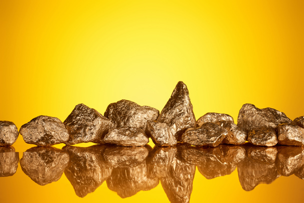 pile of gold shiny stones in row with reflection on yellow background with copy space - Фото, зображення