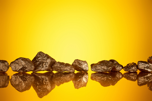 gold shiny stones in row with reflection on yellow background with copy space - Foto, Bild