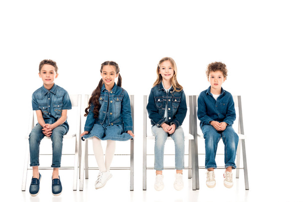 four kids in denim clothes sitting on chairs on white - Zdjęcie, obraz