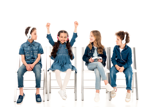 four kids in denim clothes sitting on chairs and listening music in headphones on white - Φωτογραφία, εικόνα