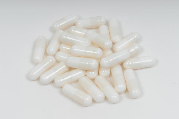 Witte pil capsules op witte achtergrond. Voedingssupplementen in de vorm van gelatinecapsules. Hyaluronzuurcapsules in een veganistische cellulosecapsule. - Foto, afbeelding
