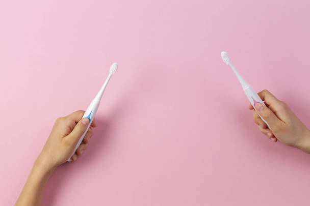 Manos de niño con cepillos de dientes eléctricos sobre fondo rosa
 - Foto, Imagen