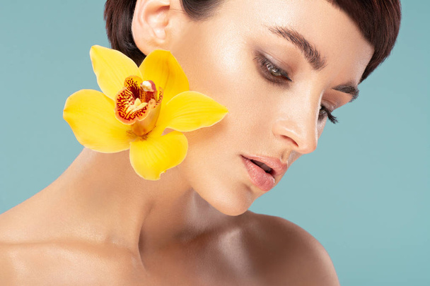 beautiful brunette with short hair and yellow daffodil on a blue background - Photo, Image