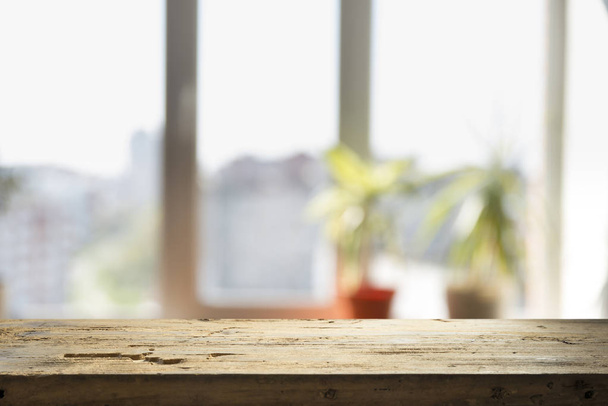 Holztischplatte auf verschwommenem Fensterglas und abstraktem Grün aus dem Garten mit Blick auf die Stadt im morgendlichen Hintergrund. für Montage Produktdisplay - Foto, Bild