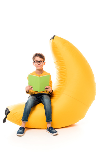 enfant en vêtements décontractés assis sur une chaise de sac de haricot et livre de lecture sur blanc
 - Photo, image