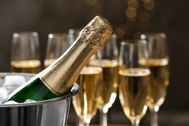 Bottle of champagne in bucket with ice and glasses on blurred background, closeup. Space for text - Photo, Image