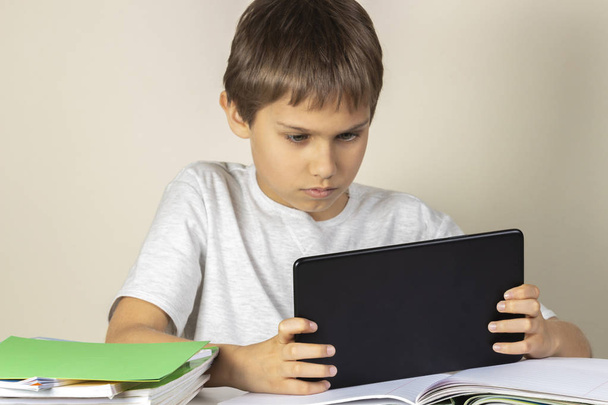 Criança sentada à mesa com cadernos de livros e usando computador tablet
 - Foto, Imagem